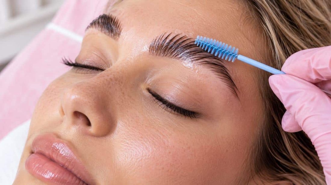 Blue spoolie brushing glossy laminated brow hairs upward